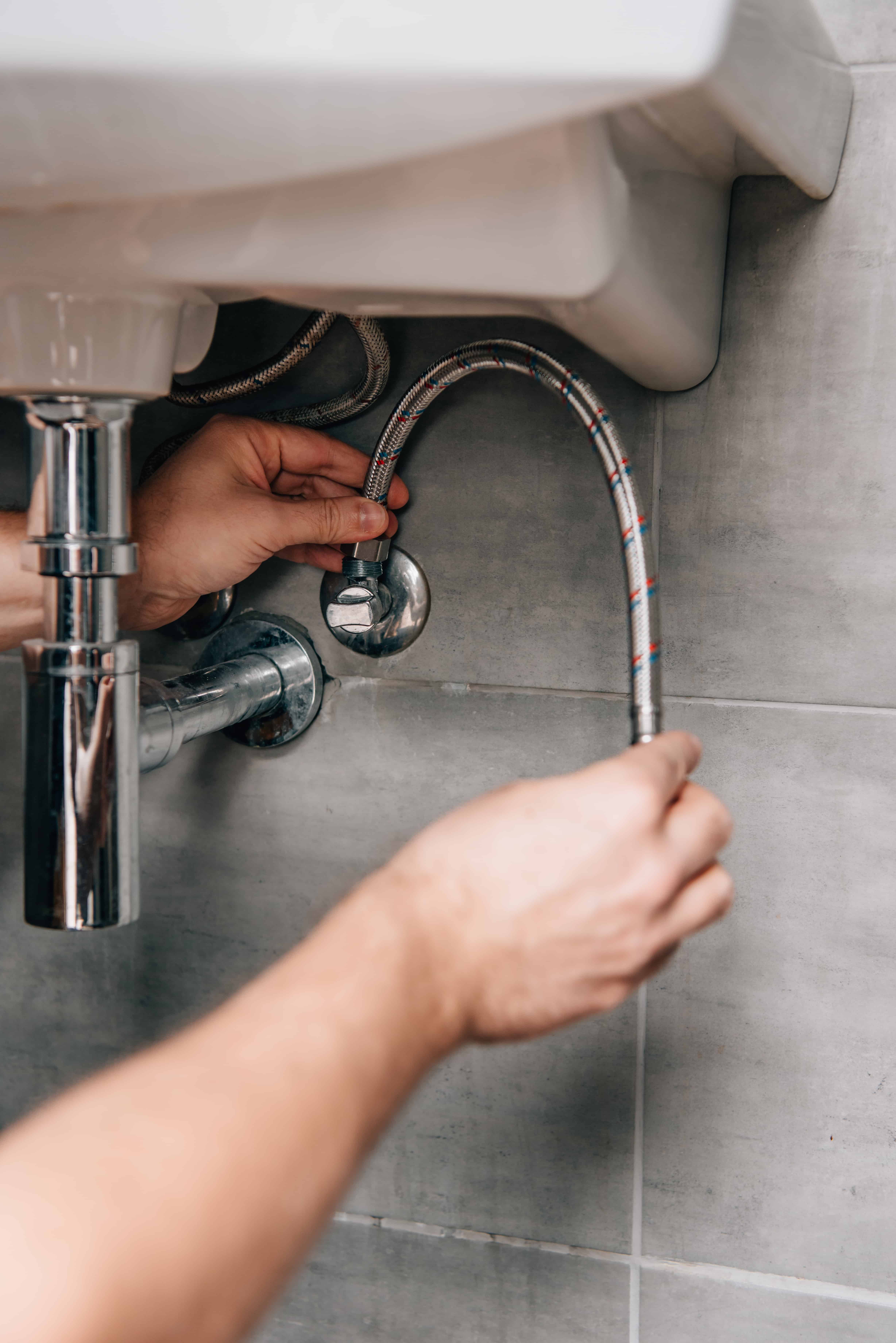 Plumber fitting flexible hoses under a bathroom sink